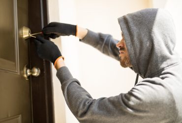 Profile view of a man with a hoodie trying to pick a lock in a house and forcing his entry